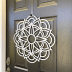 Close-up side white mandala metal wreath on dark wood door, handcrafted floral wall decor, modern outdoor metal sign, elegant entryway design