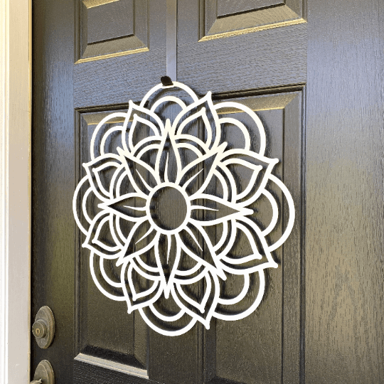 Close-up side white mandala metal wreath on dark wood door, handcrafted floral wall decor, modern outdoor metal sign, elegant entryway design