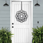 Handcrafted metal flower wreath on white door, black floral design, green plants, outdoor lights, modern entryway decor, custom metal wall art