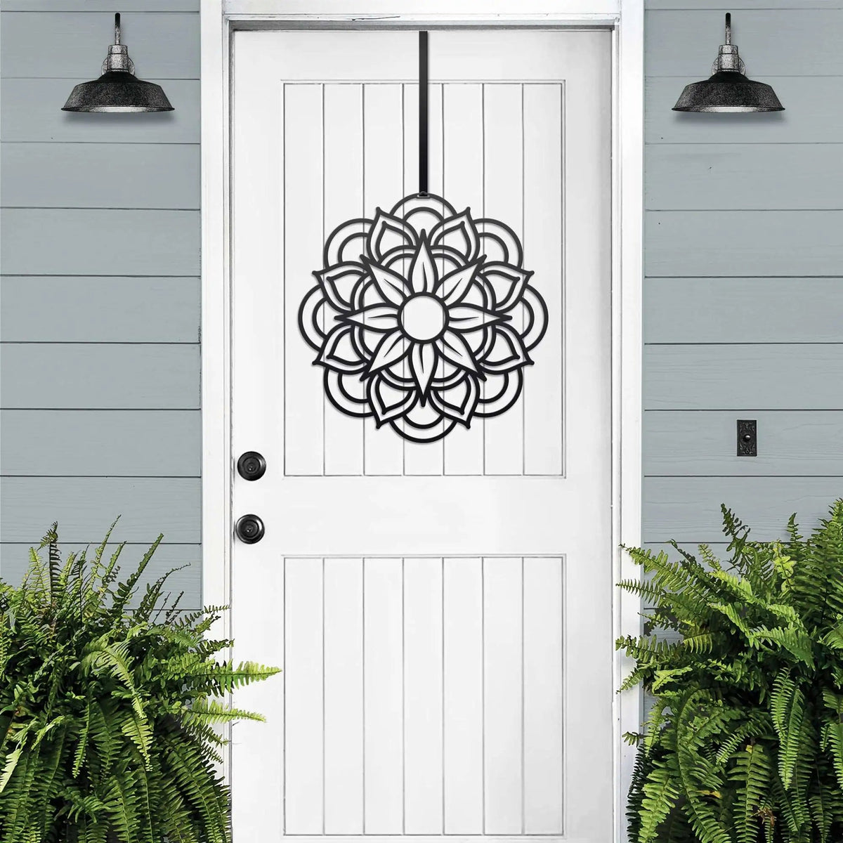 Handcrafted metal flower wreath on white door, black floral design, green plants, outdoor lights, modern entryway decor, custom metal wall art