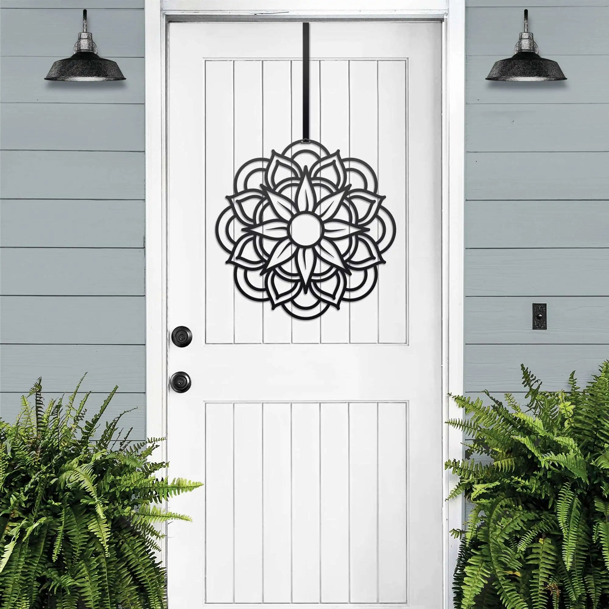 Handcrafted metal flower wreath on white door, black floral design, green plants, outdoor lights, modern entryway decor, custom metal wall art