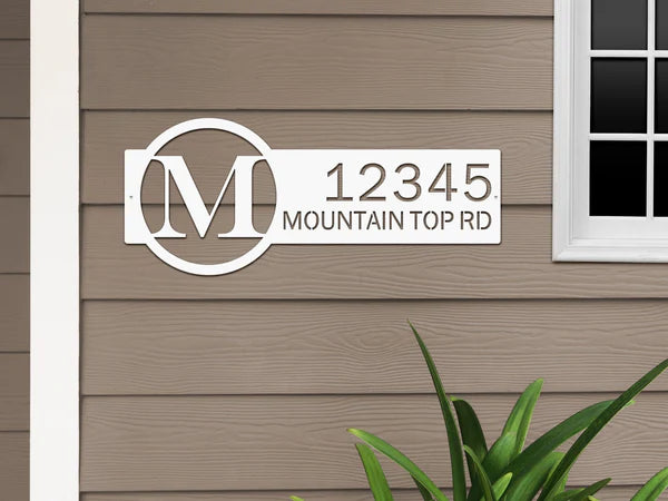 White metal monogram sign with letter 'M' and '12345 Mountain Top RD', mounted beside a door.
