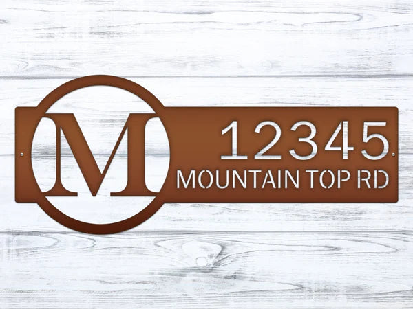 Close-up bronze metal monogram sign with letter 'M' and '12345 Mountain Top RD'.