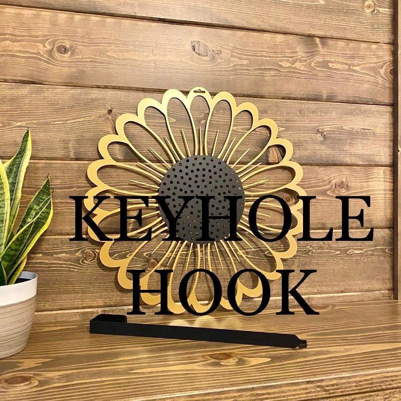 HouseSensationsArt metal over-the-door wreath and floral hanger in sunflower design, decorative keyhole hook displayed on wood, part of 90-color USA-made collection.