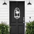Black front door with decorative white palm tree “Welcome” decal, flanked by green plants on white wall, custom outdoor home entrance décor