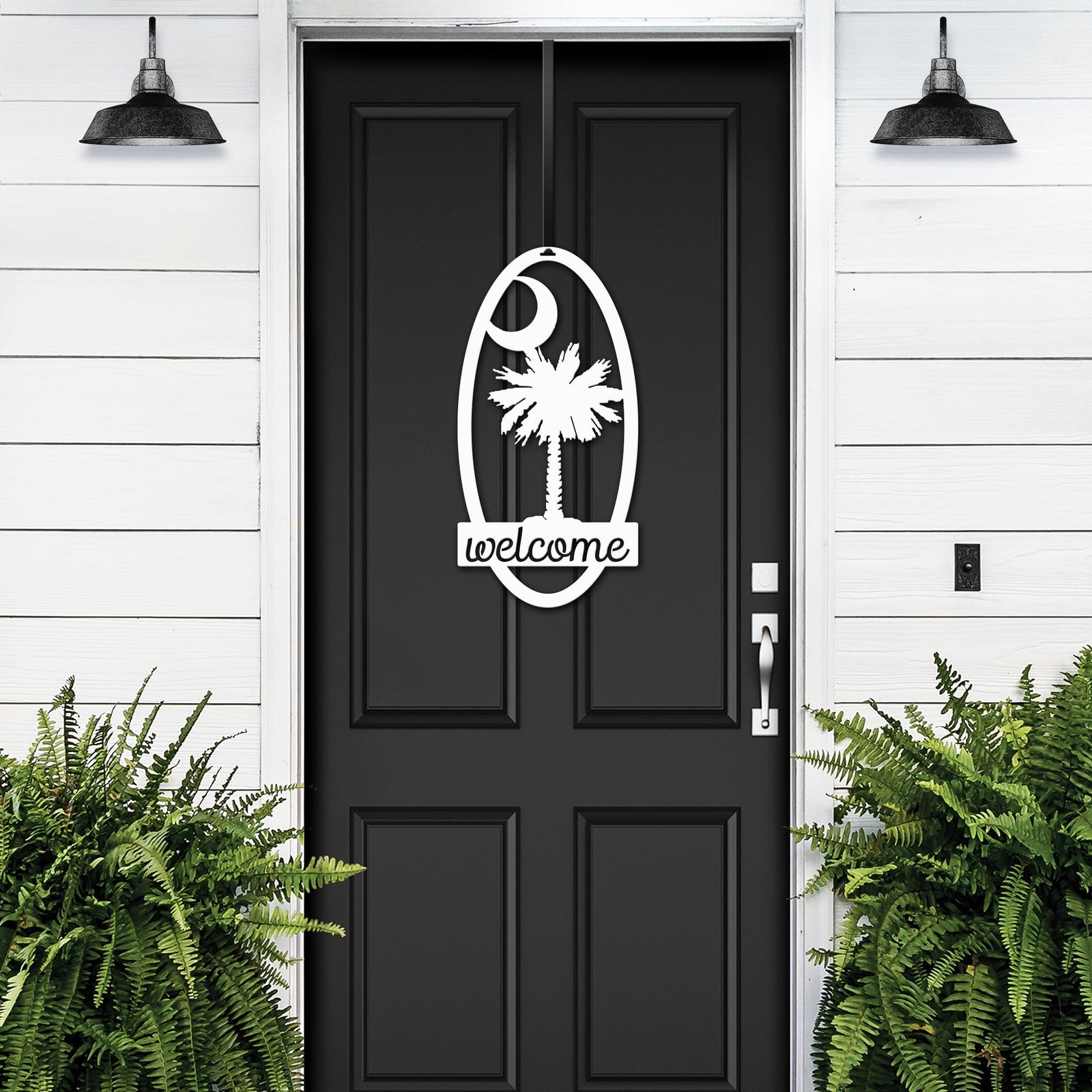 Black front door with decorative white palm tree “Welcome” decal, flanked by green plants on white wall, custom outdoor home entrance décor