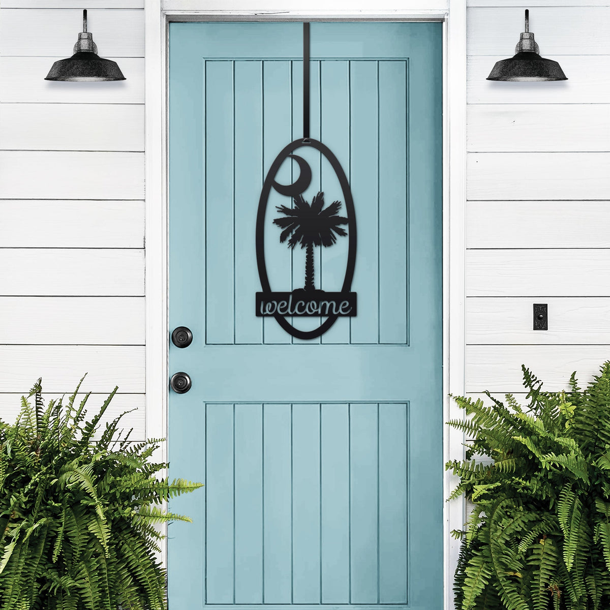Light blue door with black decorative “Welcome” decal, flanked by green plants on white wall, custom outdoor home entrance décor