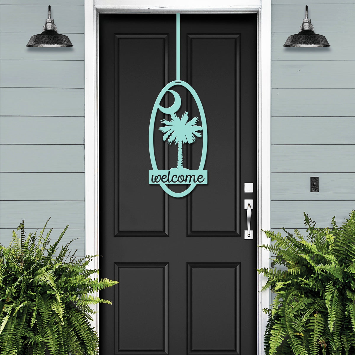 Black door with decorative palm tree “Welcome” decal, flanked by green plants against light blue wall, custom outdoor home entrance décor