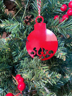 Red decorative ornament with intricate cut-out design hanging on a Christmas tree, surrounded by lush green branches, creating a festive and traditional holiday decoration scene.