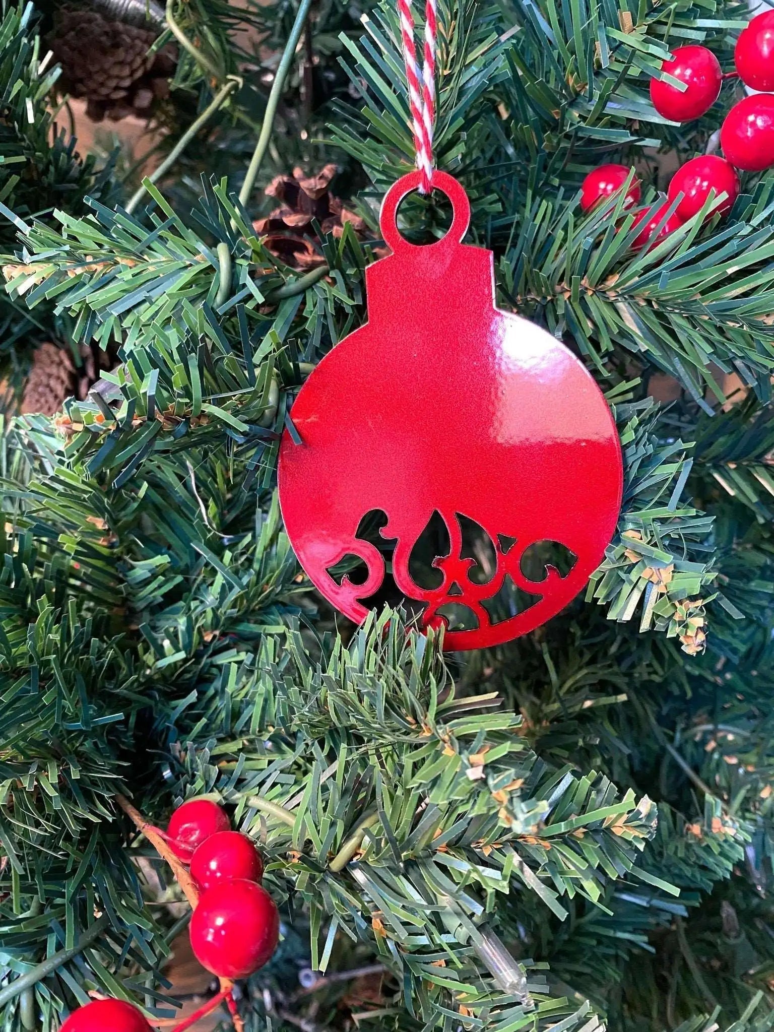 Red decorative ornament with intricate cut-out design hanging on a Christmas tree, surrounded by lush green branches, creating a festive and traditional holiday decoration scene.