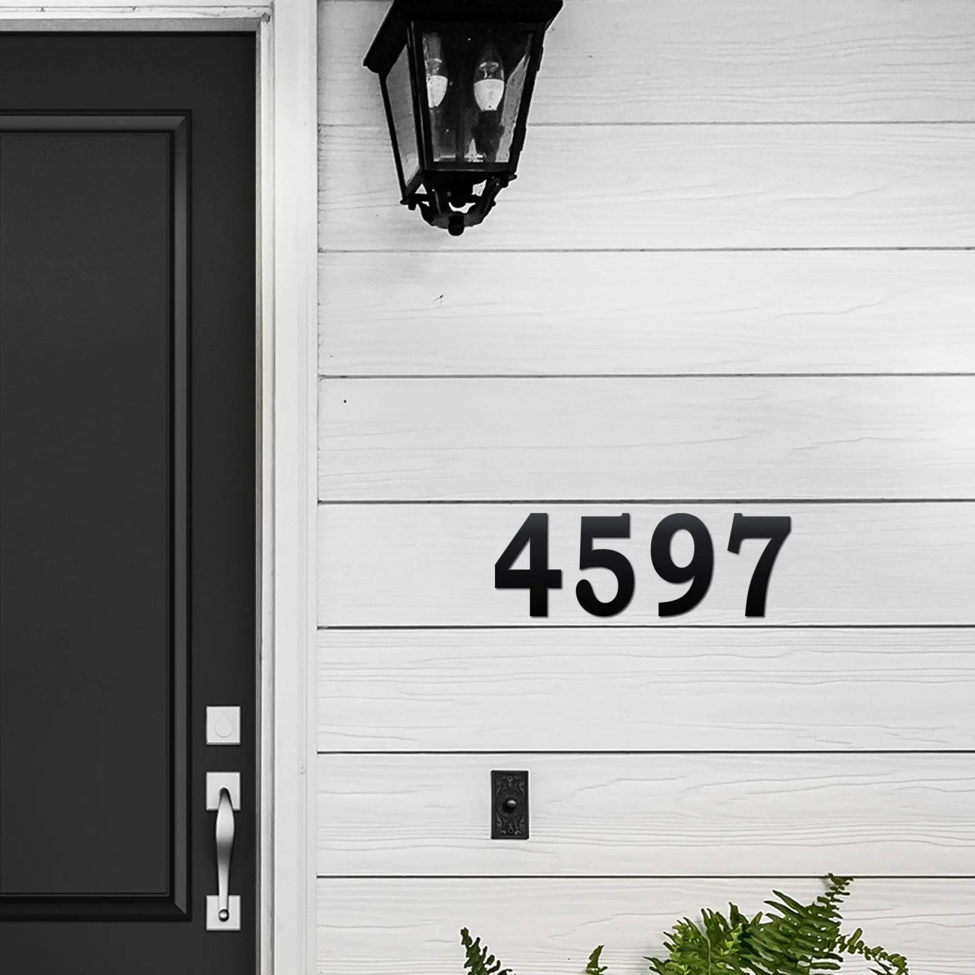 House exterior with black door and custom black metal house numbers “4597” mounted on a white wall for personalized address signage and decorative outdoor metal signs