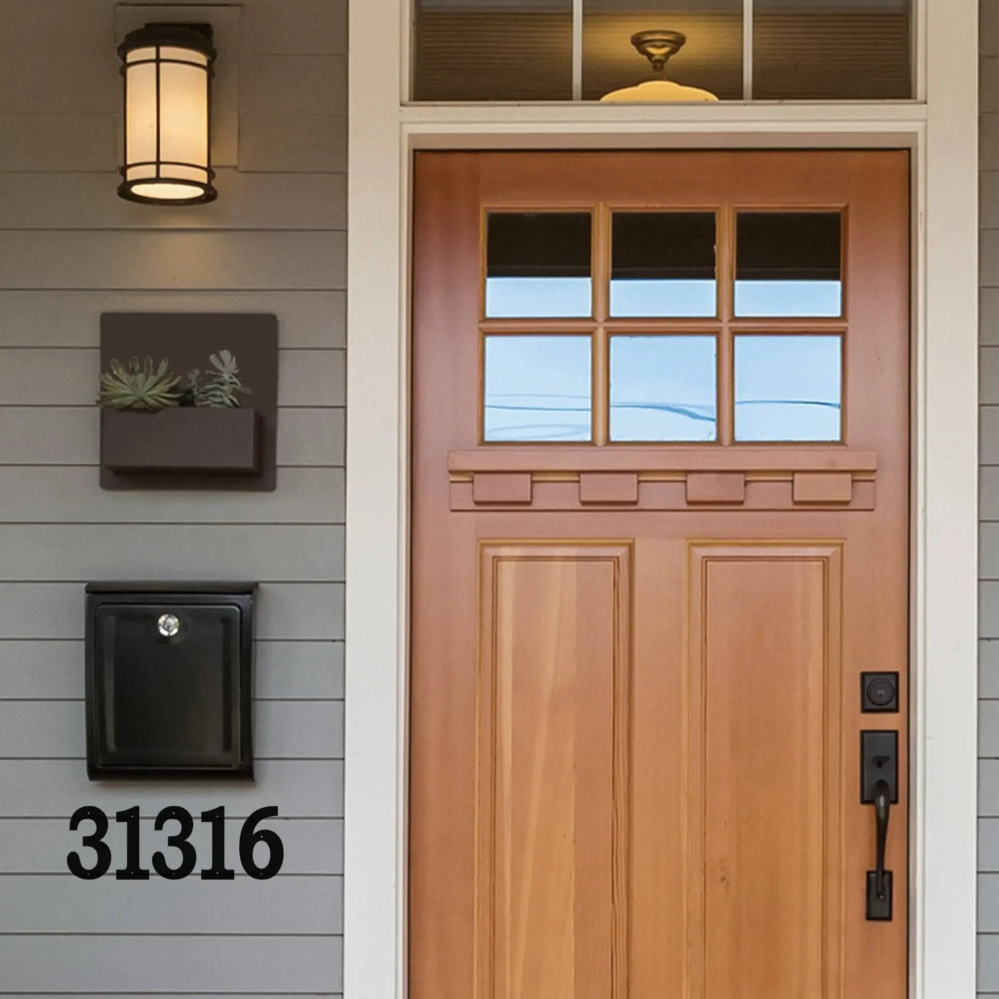 Wooden front door with glass panels, mail slot, and black metal address numbers on gray house exterior for custom house number signage and personalized outdoor décor