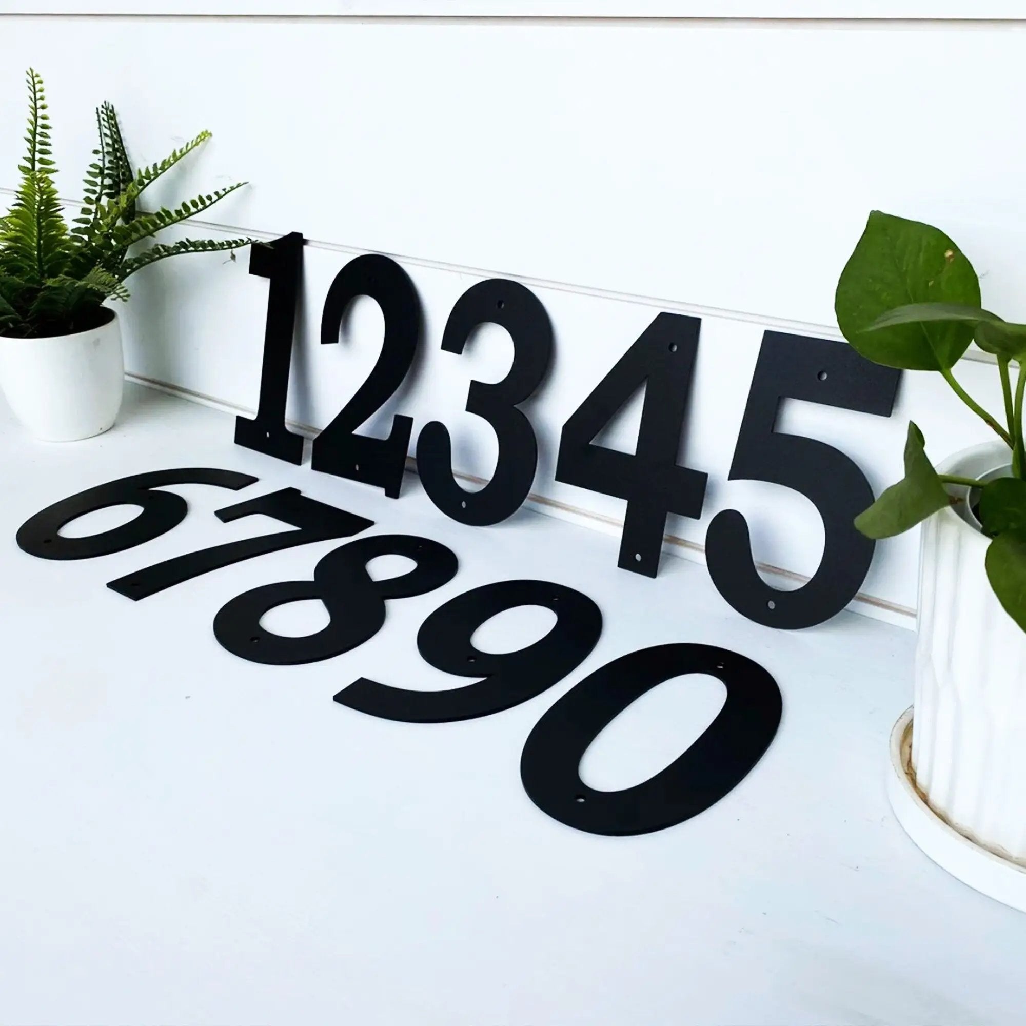 Black metal house numbers displayed on a white surface with greenery for custom address signs, personalized home décor, and decorative outdoor signage