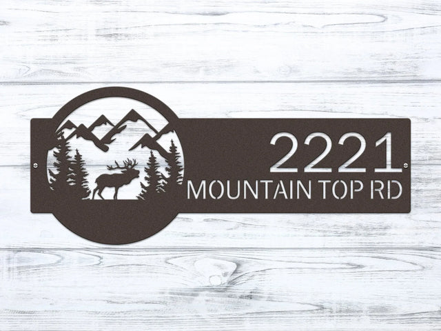 Oil-rubbed bronze Mountain Elk Address Sign featuring elk, pine trees, and mountain on the right, with house number '2221 Mountain Top Rd' on the left, mounted on the door wall.