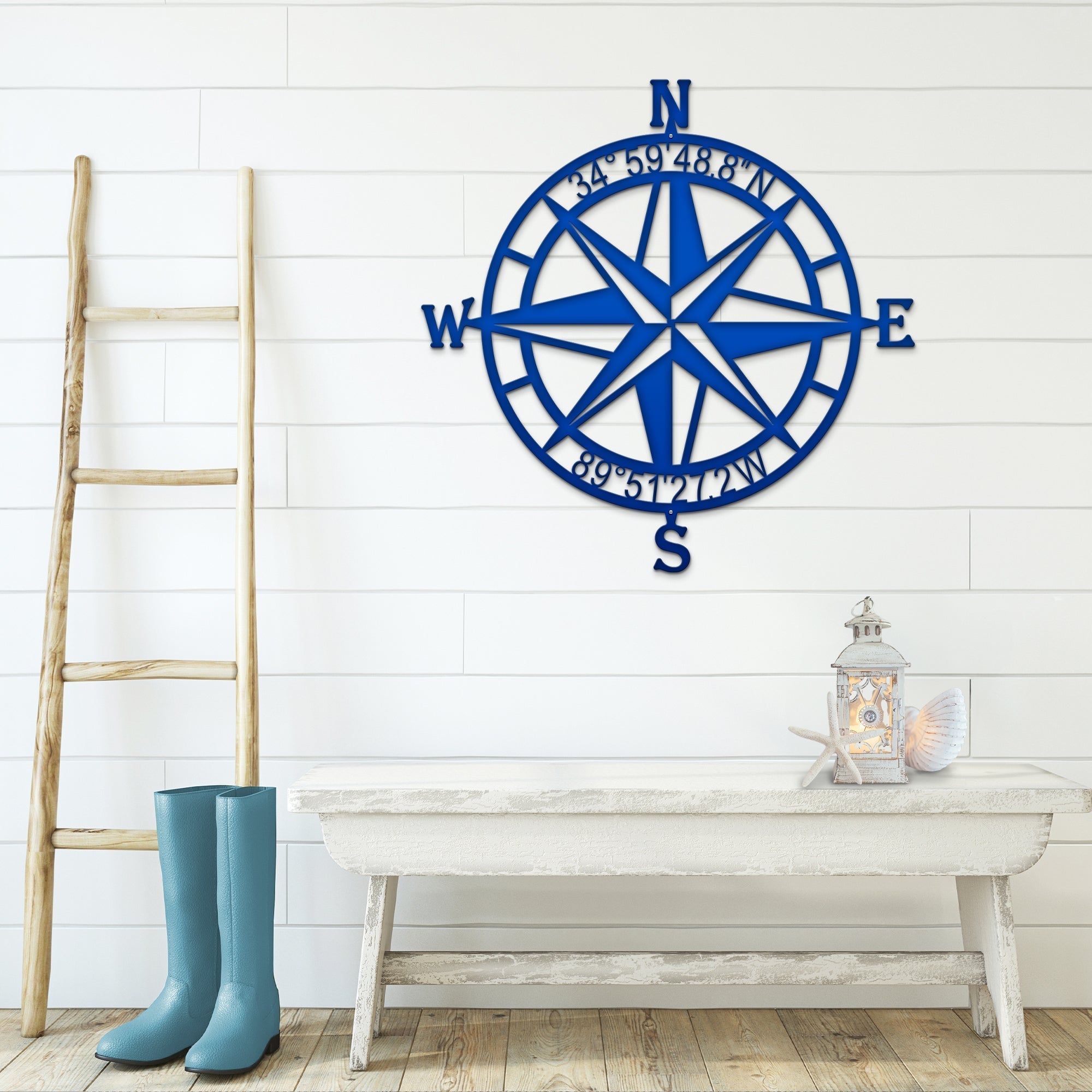 Blue nautical compass rose metal wall décor on white wall with wooden ladder and table in foreground, coastal-inspired décor, HouseSensationsArt