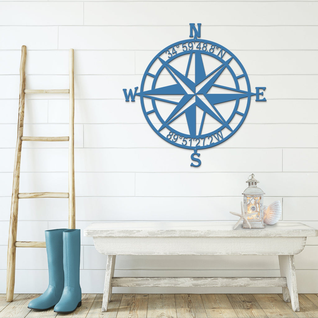Blue nautical compass rose metal wall décor on white wall with wooden ladder and table in foreground, coastal-inspired décor, HouseSensationsArt
