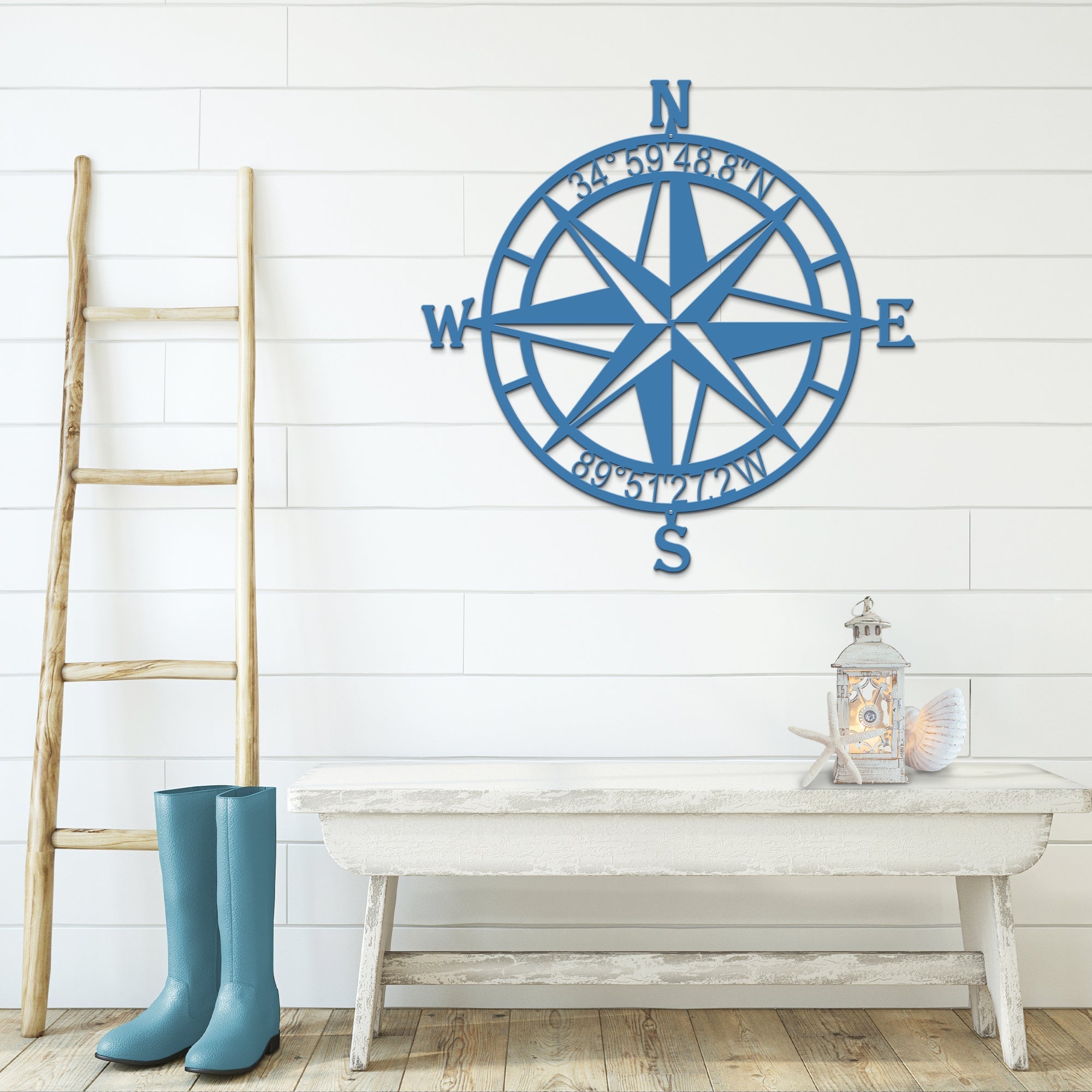 Blue nautical compass rose metal wall décor on white wall with wooden ladder and table in foreground, coastal-inspired décor, HouseSensationsArt