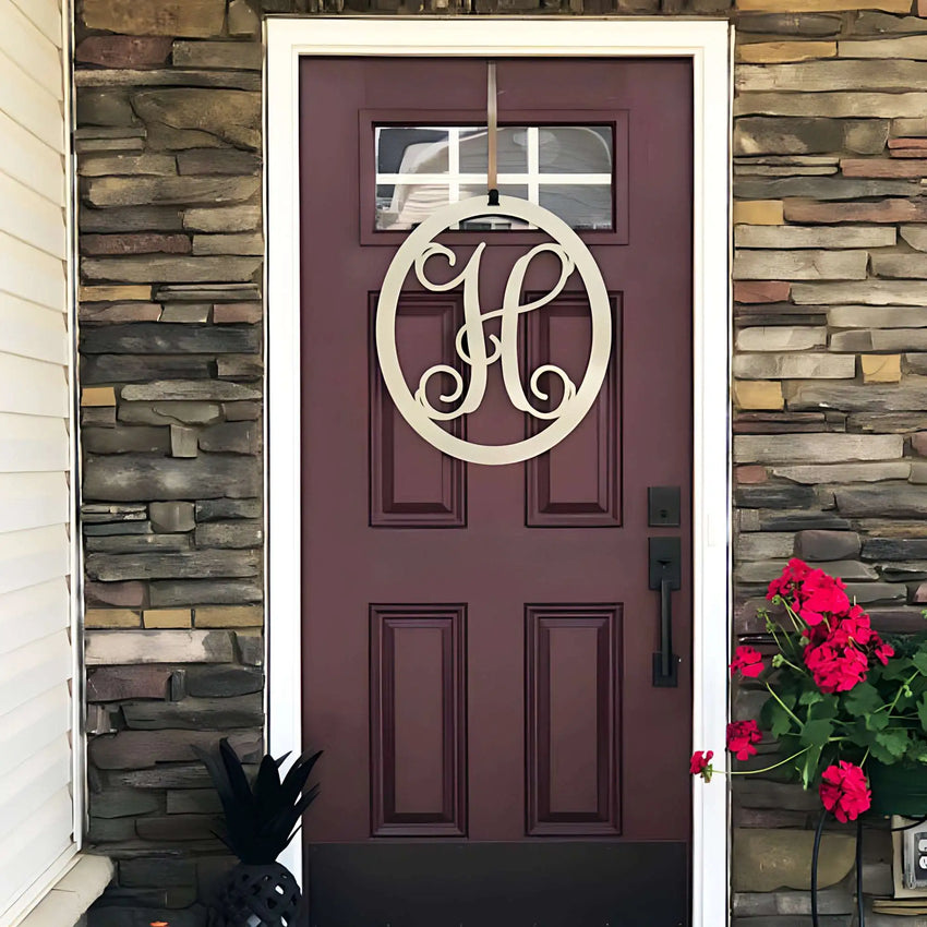 Beige oval metal monogram door wreath shown on a maroon door