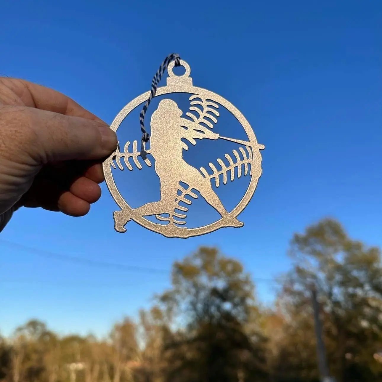 Metallic ornament featuring silhouette of person holding a fish against blue sky, fishing-themed decorative ornament for outdoor or holiday display