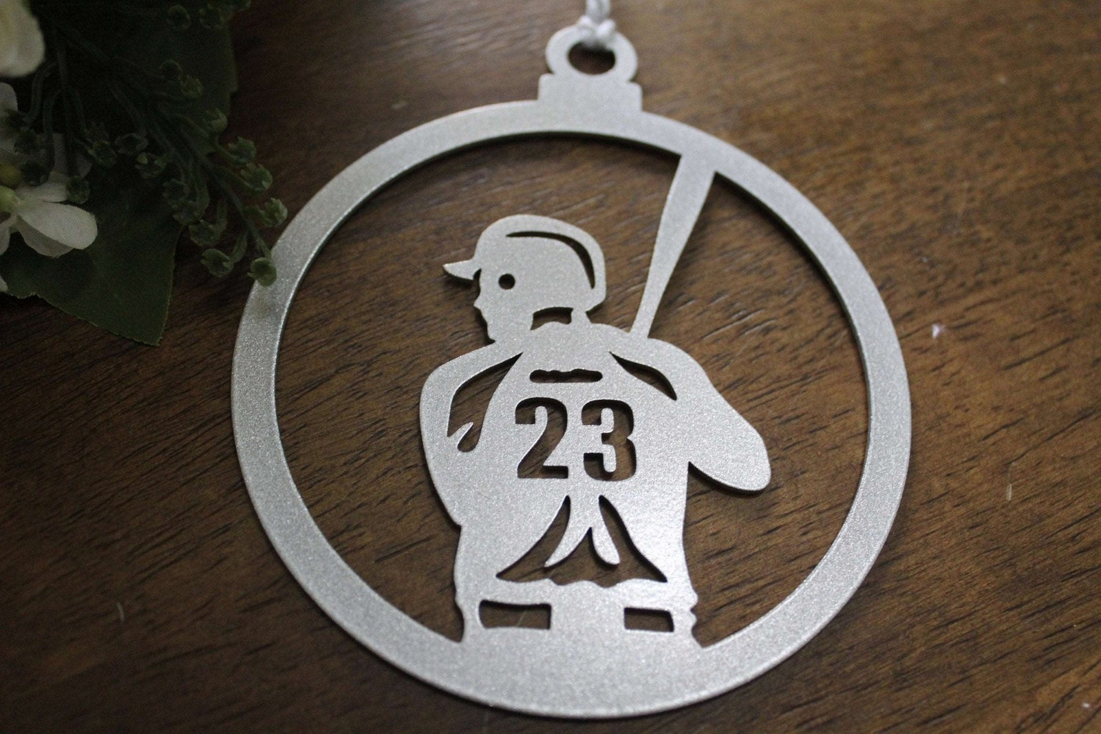 Metallic ornament with cut-out design of person on a swing featuring number 23, placed on wooden surface, decorative holiday or commemorative ornament for seasonal décor