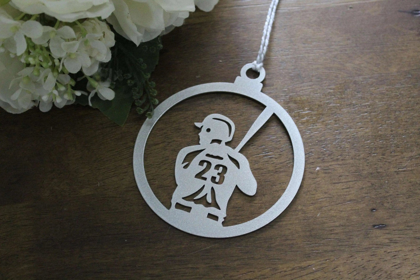 Metallic pendant featuring design of person holding number 23, displayed on wooden surface with flowers, decorative keepsake or commemorative ornament for gifts and seasonal décor
