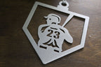 Metallic ornament featuring silhouette of person running with number 23, placed on wooden surface, decorative sports-themed ornament for holiday or commemorative display