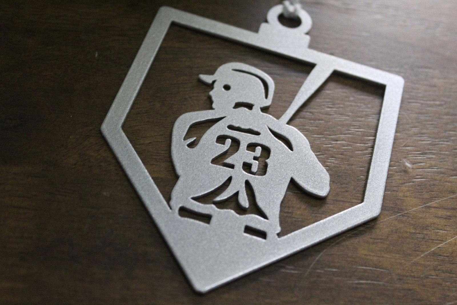 Metallic ornament featuring silhouette of person running with number 23, placed on wooden surface, decorative sports-themed ornament for holiday or commemorative display