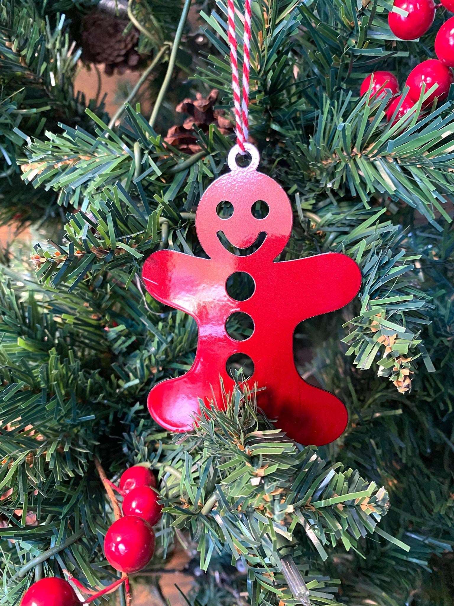 Red gingerbread man ornament hanging on Christmas tree with green leaves and red berries, festive holiday decoration for seasonal décor