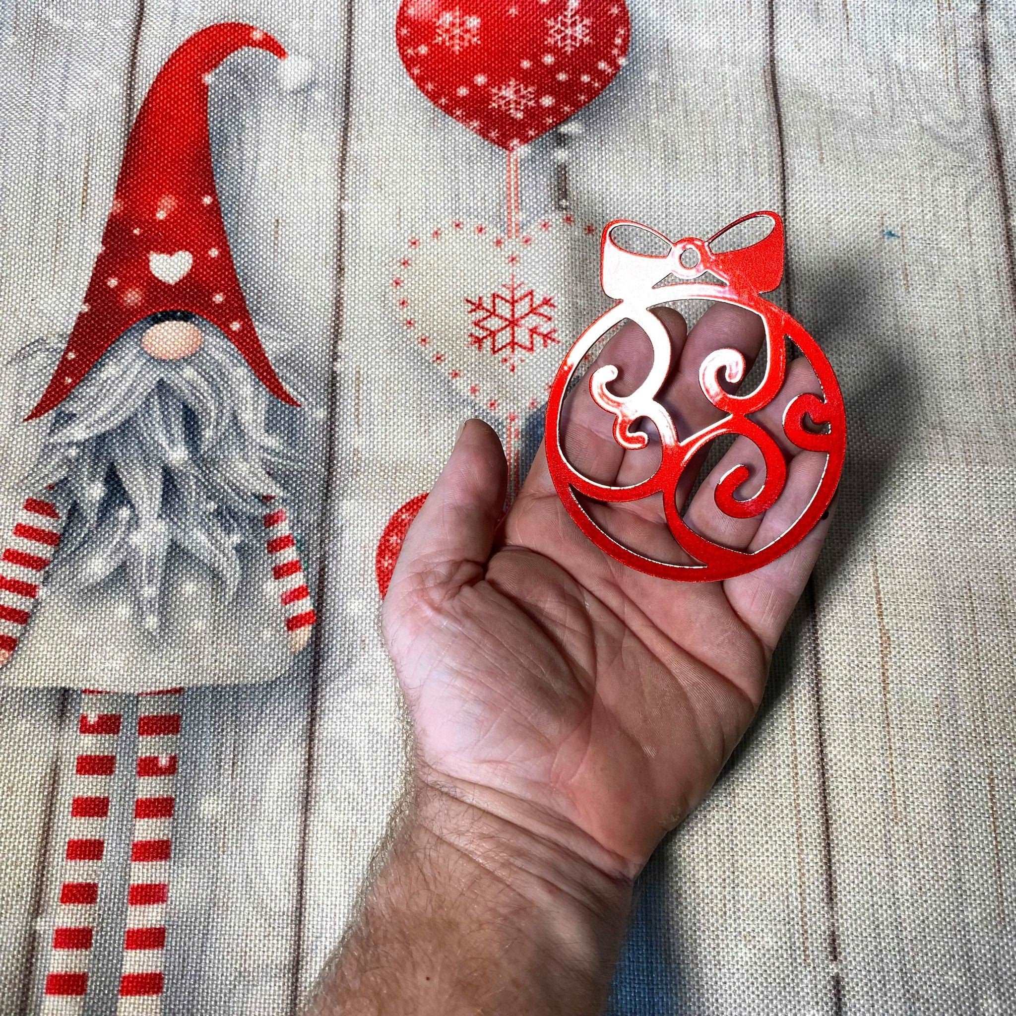 Hand holding red decorative ornament with Christmas-themed background featuring gnome and snowflakes, festive holiday decoration for seasonal décor and gift display