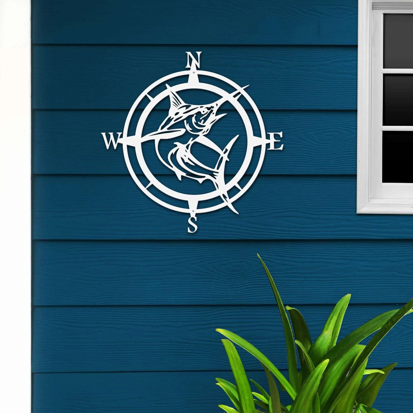 White compass design on blue wooden wall with plant in foreground, nautical decorative wall art, outdoor home exterior accent