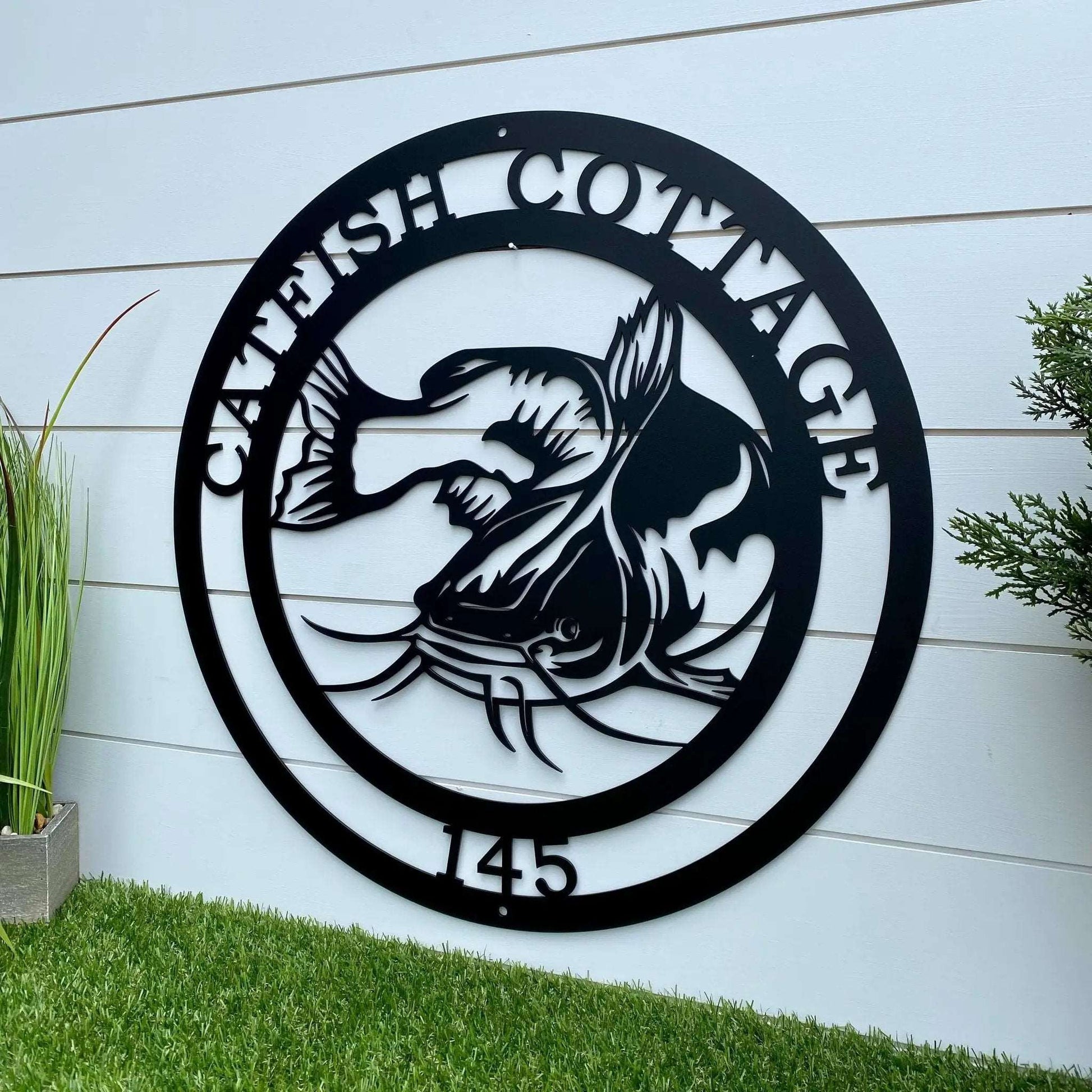 Outdoor black metal sign with catfish silhouette and “CATFISH COTTAGE 145” great for anglers' retreat decor.