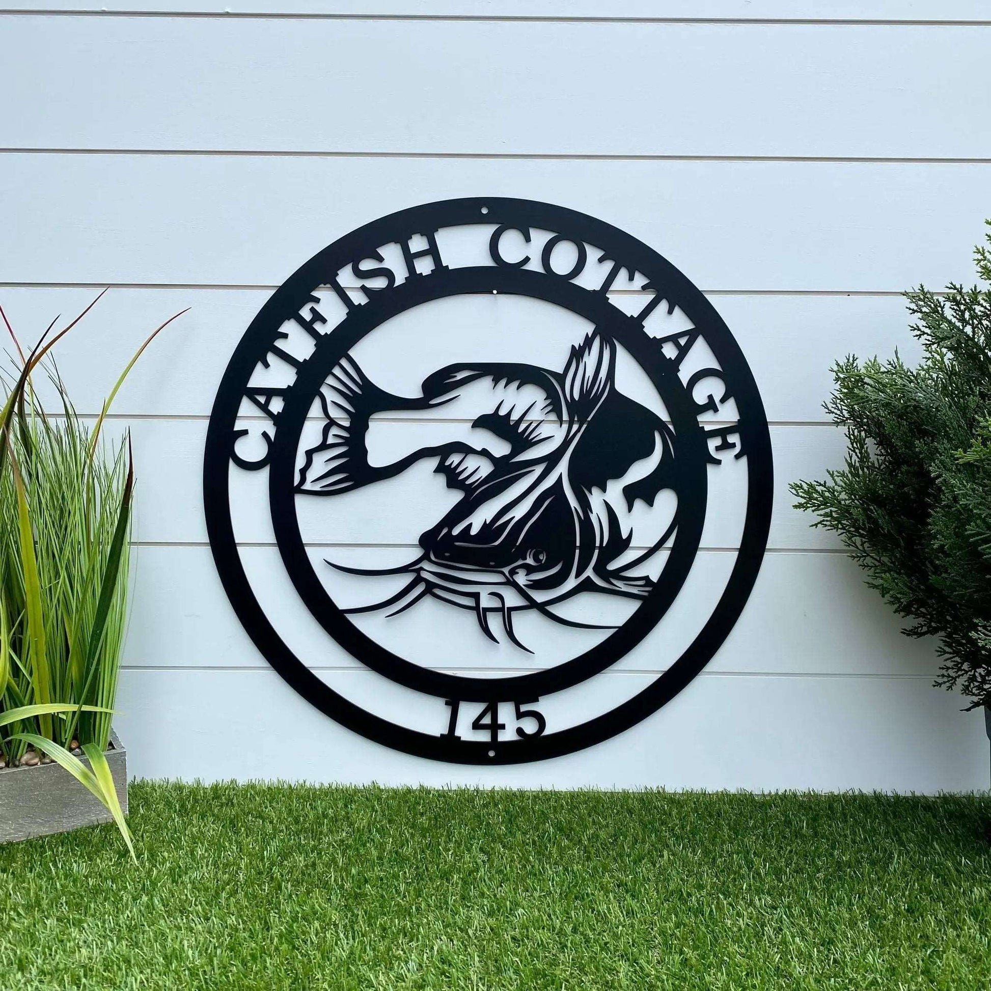 Black metal wall plaque with catfish and “CATFISH COTTAGE 145” perfect accent for any fishing lodge.