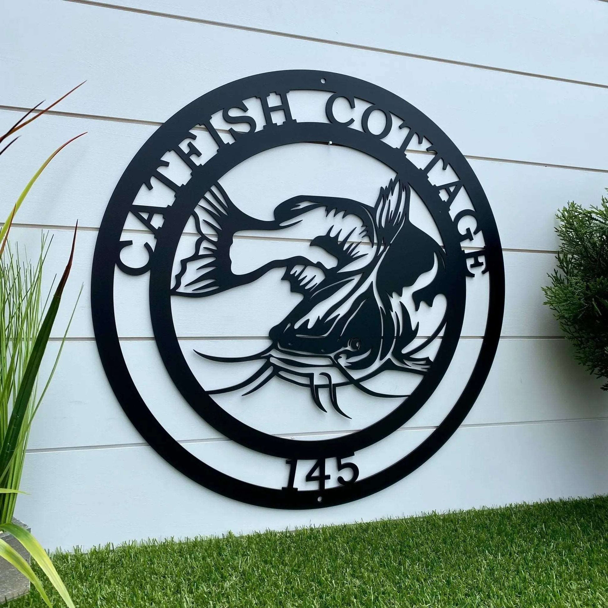 Laser-cut black metal art with catfish design and “CATFISH COTTAGE 145” great for rustic fishing cabin decor.