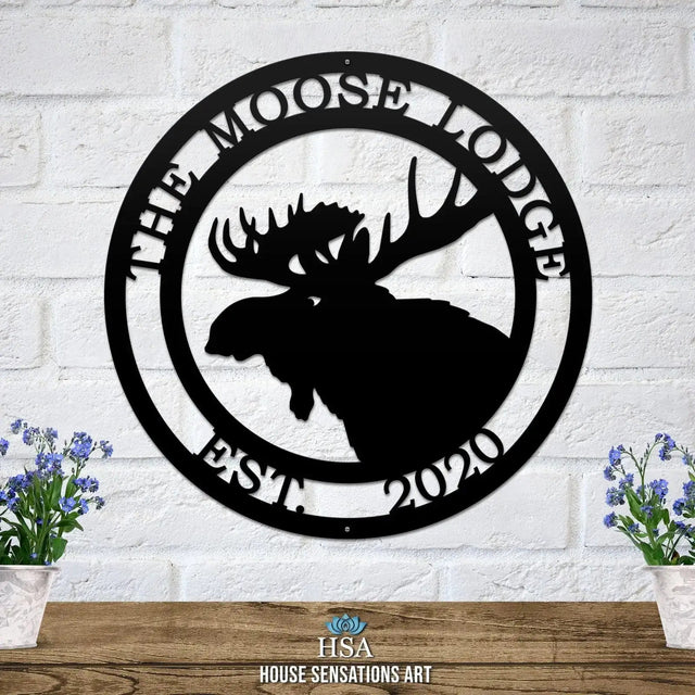 Black circular metal sign on white brick wall with moose head silhouette, "THE MOOSE LODGE" above and "EST. 2020" below in border.