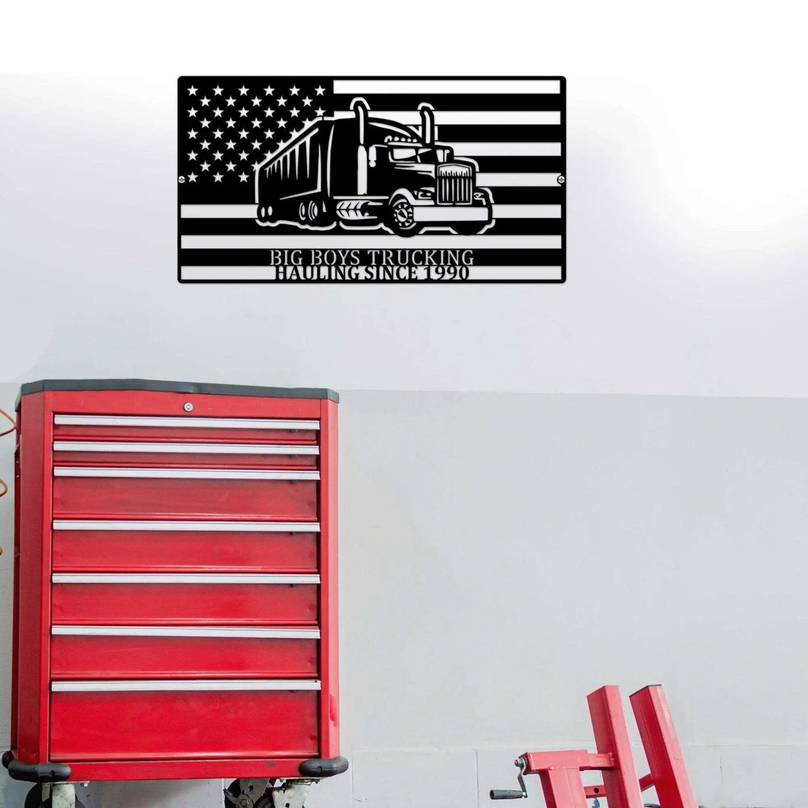 Metal wall art featuring truck design and American flag on white wall, displayed above red toolbox, patriotic decorative signage for garage or workshop décor