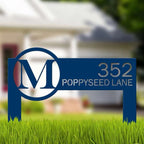 Blue metal address sign displaying “352 Poppyseed Lane” positioned on grass with a blurred house in the background, highlighting clear numbering and decorative outdoor design.
