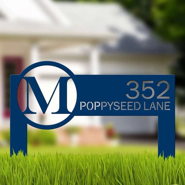 Blue metal address sign displaying “352 Poppyseed Lane” positioned on grass with a blurred house in the background, highlighting clear numbering and decorative outdoor design.