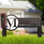 Metal address sign featuring an “M” logo and the number “352” placed on grass in front of a house, highlighting durable construction and clear, decorative outdoor display.