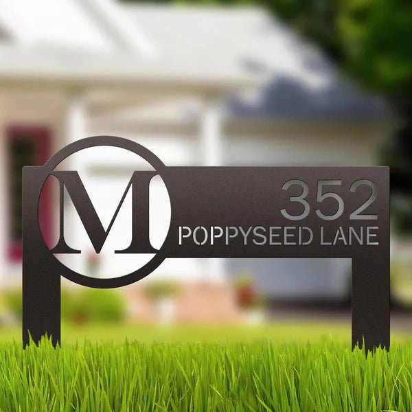 Metal address sign featuring an “M” logo and the number “352” placed on grass in front of a house, highlighting durable construction and clear, decorative outdoor display.