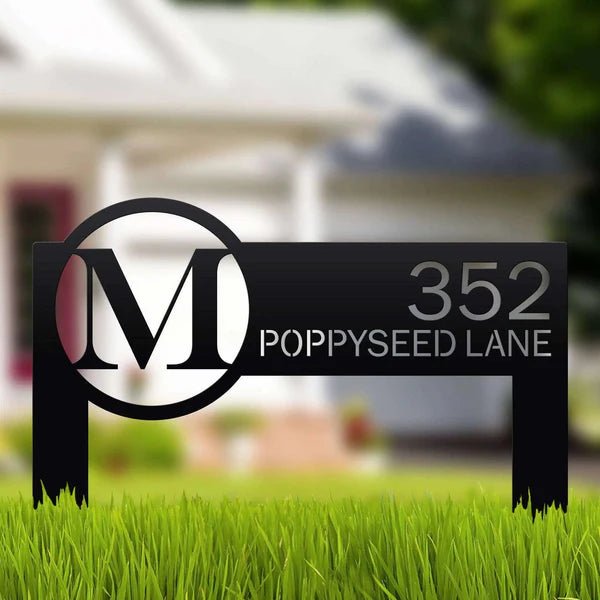 Metal address sign featuring an “M” logo displayed on grass in front of a house, highlighting durable craftsmanship and decorative outdoor appeal.