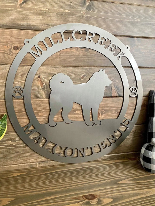 Polished chrome metal yard sign with dog silhouette, “MILLCREEK” text, and paw prints; mounted on paneled wall.