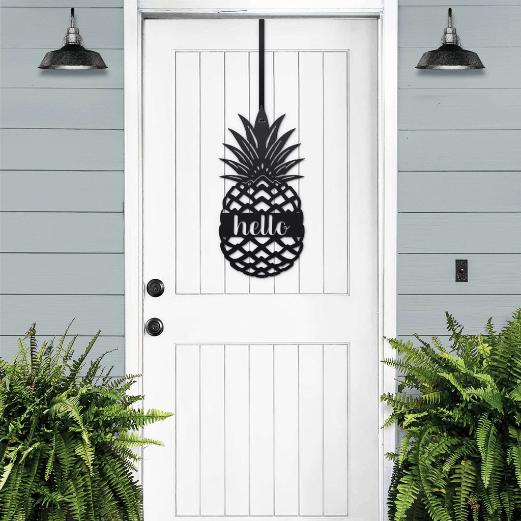 White front door with black pineapple hello metal sign decal, light blue wall and green plants, tropical farmhouse entry décor, custom powder coated welcome wall art sign