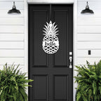 Black front door with pineapple hello metal sign decal, white wall exterior with green plants, tropical farmhouse entry décor, custom powder coated welcome wall art sign