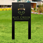 Black metal sign with Hat Creek Restoration logo on grassy outdoor background, personalized laser-cut design for business branding and decorative signage