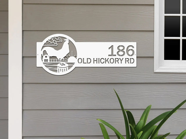 White Farm Address Sign with rooster, clouds, barn, sun on right and '186 Old Hickory Rd' on left, mounted on door wall.