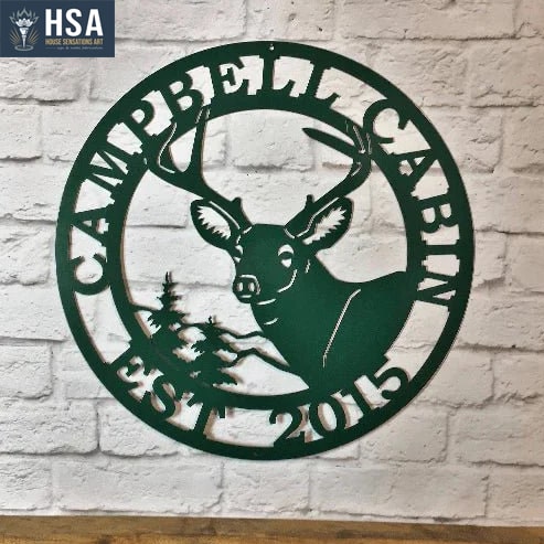 A metal sign with a deer and text saying 'Campbell Cabin EST 2025' on a white stone background
