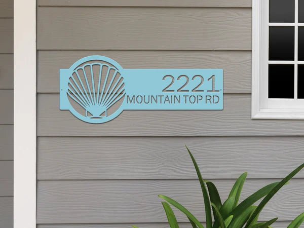 Metallic blue seashell address sign on house exterior, personalized house numbers, coastal front door décor, outdoor nautical plaque.