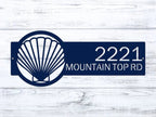 Navy blue seashell address plaque with white text on light wood background, personalized house number sign, coastal front door décor, outdoor nautical metal sign