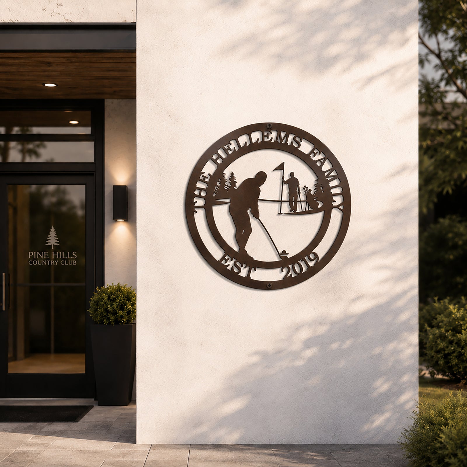 Rich espresso brown finish of the personalized golf metal art sign mounted on a white exterior stone pillar beside the glass front entryway door of the Pine Hills Country Club.