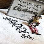 Decorative sign with Have yourself a Merry Little Christmas text and small reindeer figurine on white surface, festive holiday décor for seasonal home display